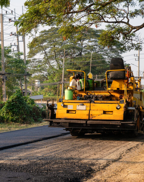 Yellow steamroller or soil compactor working on asphalt highway road at construction site